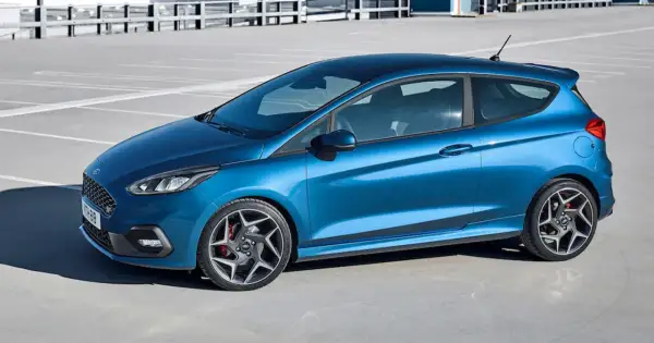 Niebieski Ford Fiesta ST z czarnym dachem i felgami stoi na parkingu.