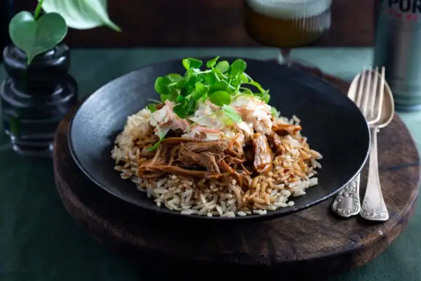 En tallrik med pulled pork med ris, toppad med krispig coleslaw och gröna blad. En härlig måltid som ser utsökt ut.