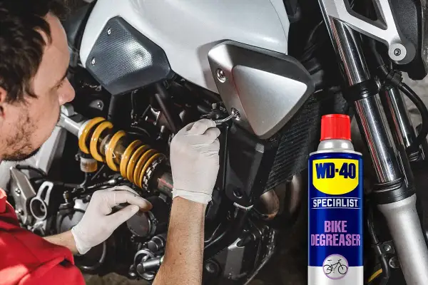 Hombre con guantes blancos trabajando en la cadena de moto. Lata de WD-40 Specialist Bike Degreaser para quitar oxido cadena moto.