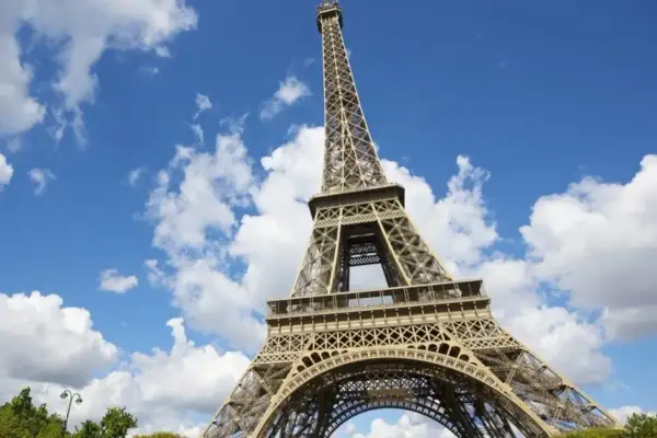 Vue en contre-plongée du برج ايفل sous un ciel bleu parsemé de nuages blancs.