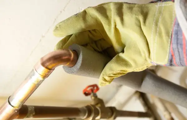 Hand mit Handschuh isoliert Kupferrohre, um Heizungsrohre zu verlegen und Energieverlust zu minimieren.