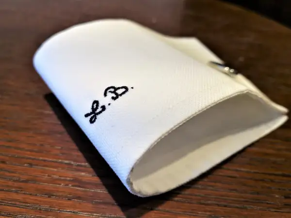 Un dettaglio di una camicia bianca piegata, con le iniziali "F.B." ricamate in nero.