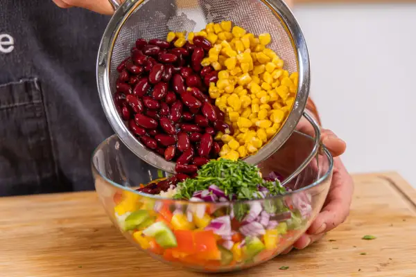 Kidneybohnen und Mais werden in eine Schüssel mit Paprika, Zwiebeln und Kräutern gegeben. Ein bunter Kidneybohnen Salat entsteht.