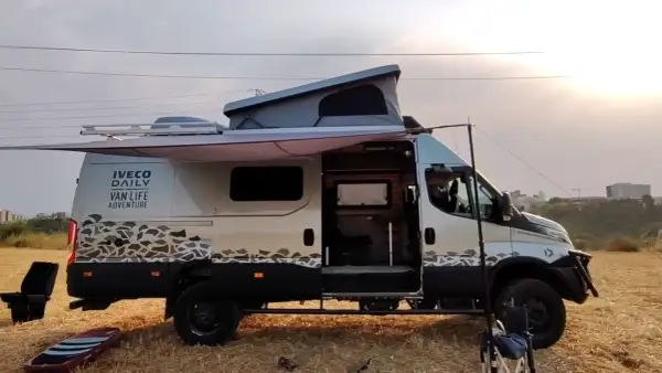 Ce **modèle camion** Iveco Daily aménagé pour le "Van Life Adventure" est prêt pour l'exploration, avec son toit relevable et son auvent déployé.