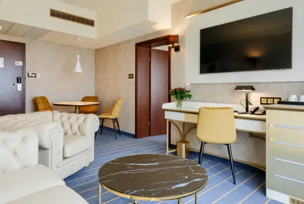 Elegancki pokój w hotelu Diament Wrocław: wygodna sofa, biurko z telefonem i TV, stolik kawowy i okrągły stół z krzesłami.