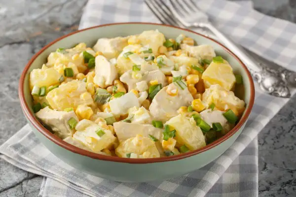 Insalata di pollo e patate cremosa con mais, uova sode e cipollotto fresco, servita in una ciotola verde.