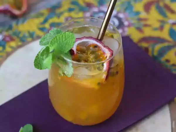 Un délicieux cocktail thé glacé aux fruits de la passion, garni de menthe fraîche et d'une tranche de fruit.