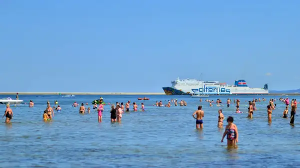 Ludzie kąpią się w morzu, a w tle płynie prom Polferries, który kursuje na trasie Świnoujście - Ystad.