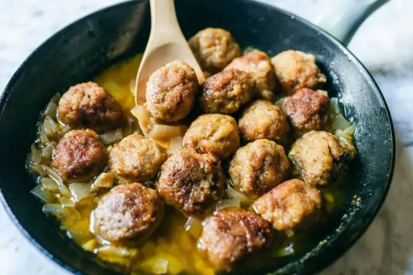 Polpette in bianco dorate e succulente, cotte in padella con cipolle dolci e un sughetto invitante. Un classico confortante.