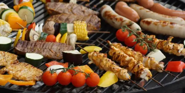 Na ruszcie grilluje się zdrowy grill: szaszłyki z kurczaka, wołowiny i warzyw, kiełbaski, pomidorki i kukurydza.