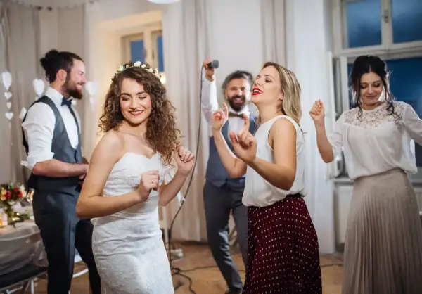 Brautpaar und Gäste tanzen ausgelassen. Frauen im lässigen Chic auf einer Hochzeit, die Braut trägt ein Spitzenkleid.