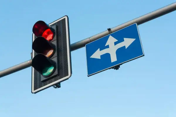 Czerwone światło na sygnalizatorze i znak wskazujący kierunki jazdy. Pamiętaj, co grozi za przejazd na czerwonym świetle – mandat i punkty karne.