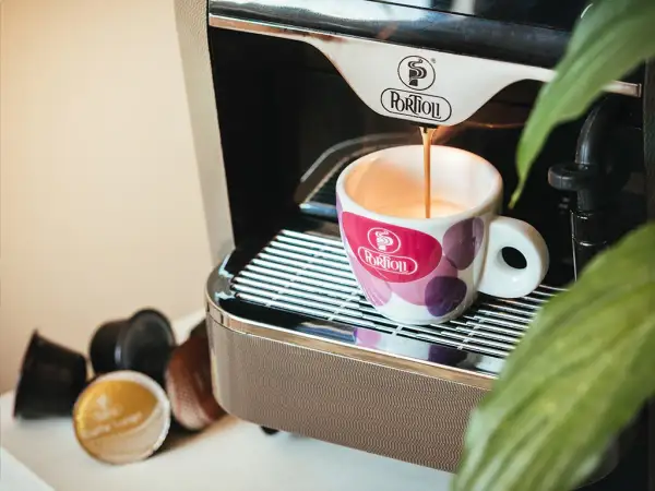 Espresso pouring into a patterned cup next to coffee capsules and a coffee machine.