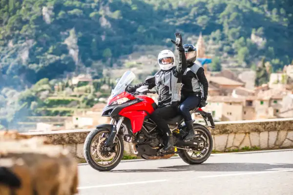 Para jadąca na czerwonym motocyklu Ducati, z pasażerem pozdrawiającym ręką.