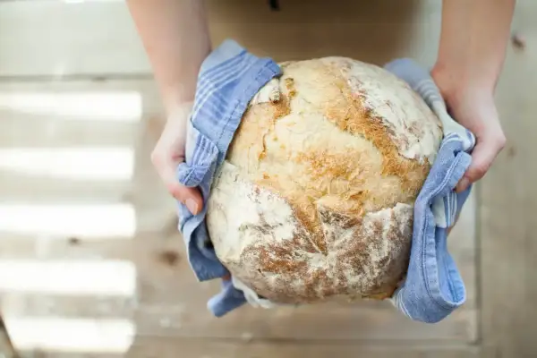 Mains d'une personne tenant un pain artisanal doré, tout juste sorti du four. Une belle réussite de recette pain.