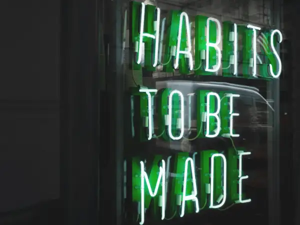 Zielone neony "HABITS TO BE MADE" przypominają o psychologii systemu nagród i kar, który kształtuje nasze nawyki.
