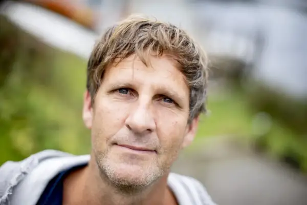En snygg dansk skådespelare med blont, rufsigt hår och blå ögon ler mot kameran utomhus.