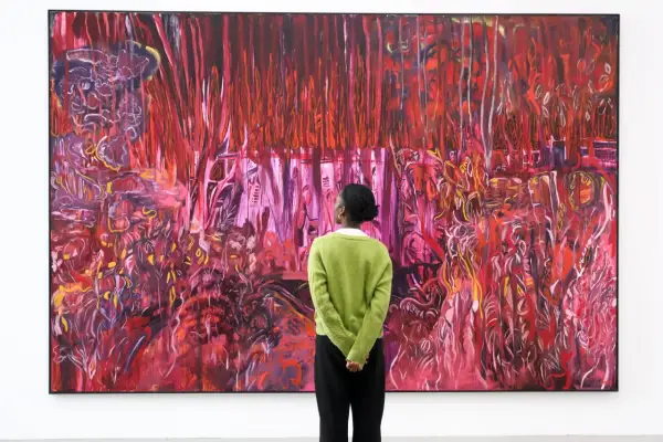A person in a green sweater contemplates a vibrant, abstract painting, a visual guide on how to find up and coming artists.