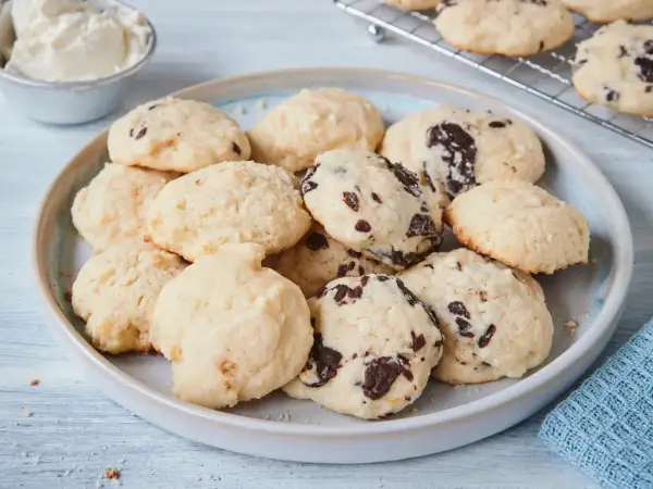 Leckere Cheesecake Cookies mit Schokoladenstückchen auf einem Teller, daneben eine Schüssel Frischkäse.
