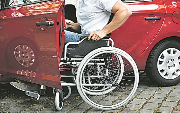 Un uomo in carrozzina si prepara a salire in un'auto rossa. Un caregiver ha aiutato nell'acquisto di un'auto adatta.