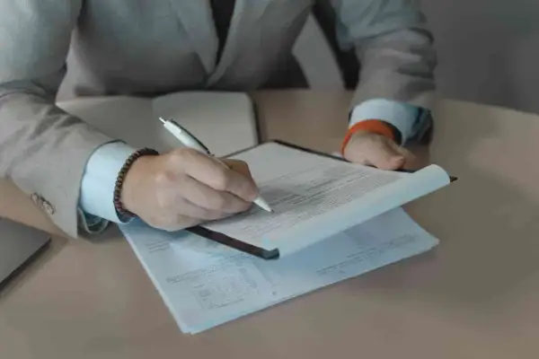 Rekruter w garniturze podpisuje dokumenty. Praca rekrutera to często analiza CV i rozmowy.