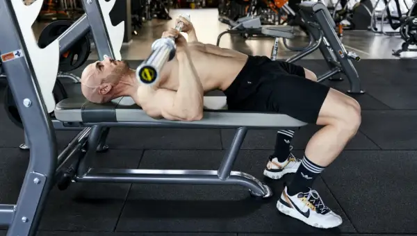 Uomo calvo si allena in palestra, sollevando un bilanciere su una panca. Un esempio di **super serie palestra** per un allenamento intenso.