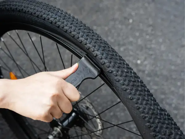 Dłoń używa czarnej łyżki do opon rowerowych, aby zdjąć oponę z obręczy. To pokazuje, jakie łyżki do opon rowerowych są potrzebne do naprawy.