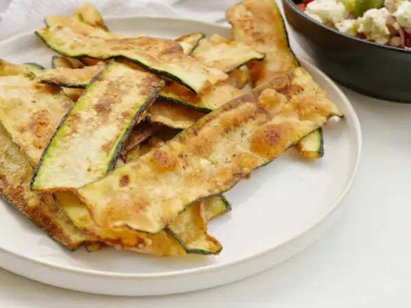 Krispiga, gyllene skivor av friterad zucchini ligger staplade på en vit tallrik, redo att avnjutas som ett lätt tilltugg.