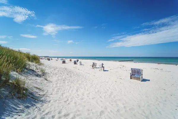 Ein sonniger Hiddensee Strand mit vielen Strandkörben, feinem Sand und dem blauen Meer.