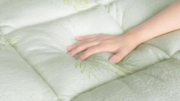 A hand rests on a quilted, light green mattress with a subtle bamboo leaf pattern. Experience the comfort and breathability of bamboo sleeping mat benefits.