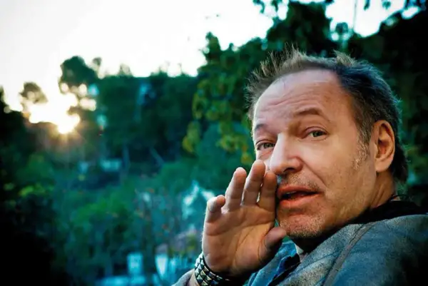 Vasco Rossi sussurra "ti prendo e ti porto via" con la mano all'orecchio, mentre il sole tramonta tra gli alberi.