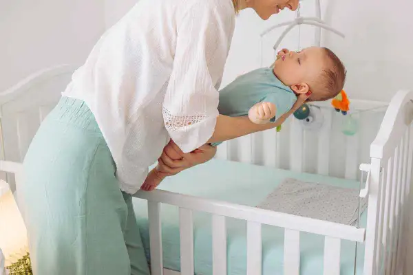 Madre acuna a su bebé dormido, listo para colocarlo en la cuna. Entender las ventanas de sueño es clave para un descanso feliz.