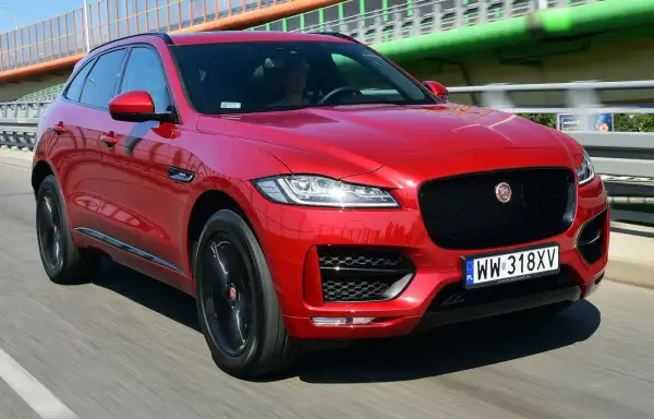 Czerwony Jaguar F-Pace na drodze. Kierowca w środku. Wiele pozytywnych jaguar f pace opinie potwierdza jego styl.