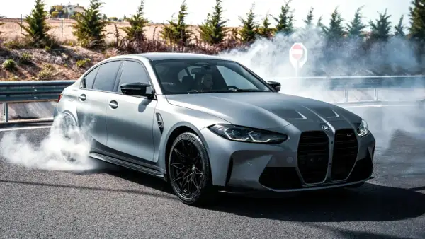 Srebrne BMW M3 G80 w poślizgu, z opon dymiących na asfalcie.