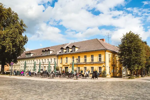 Gemütliche Straßencafés beleben die sonnige Rheinsberg Altstadt. Menschen sitzen unter grünen Sonnenschirmen vor gelben Fachwerkhäusern.