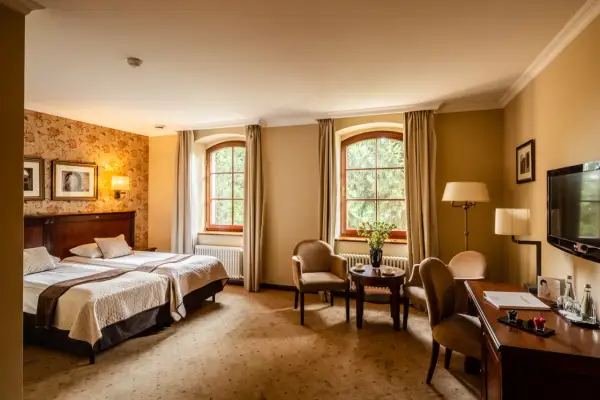 Przytulny pokój hotelowy z dwoma łóżkami, dwoma oknami i widokiem na zieleń. Idealne miejsce na wypoczynek po zwiedzaniu Wrocławia, Zamek Topacz czeka!