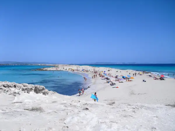 Gente disfrutando de un día soleado en las **playas blancas** con aguas turquesas y cielo azul.