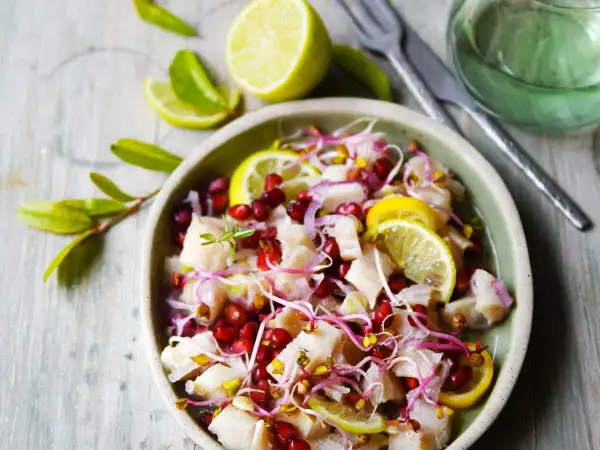 Un délicieux ceviche de poisson frais, garni de grenade, de pousses et de rondelles de citron vert.