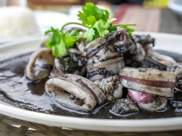 Calamares en su tinta, un plato oscuro y delicioso, adornado con cilantro fresco.