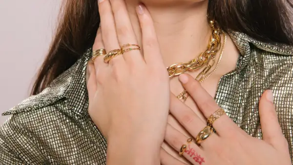 Manos adornadas con varios anillos dorados y un collar grueso, mostrando cómo llevar anillos de manera elegante.