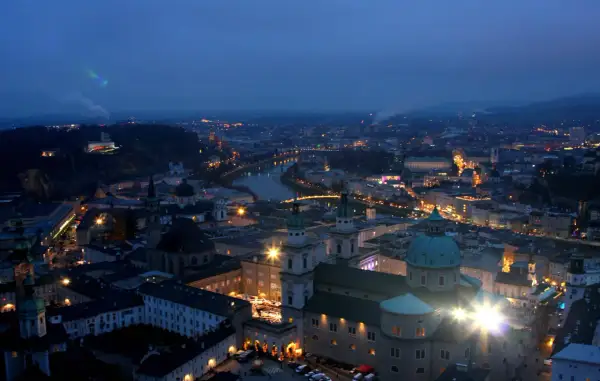 Salzburg im Winter bei Nacht. Lichter der Stadt, die Salzach und die Festung Hohensalzburg erhellen die Szene.