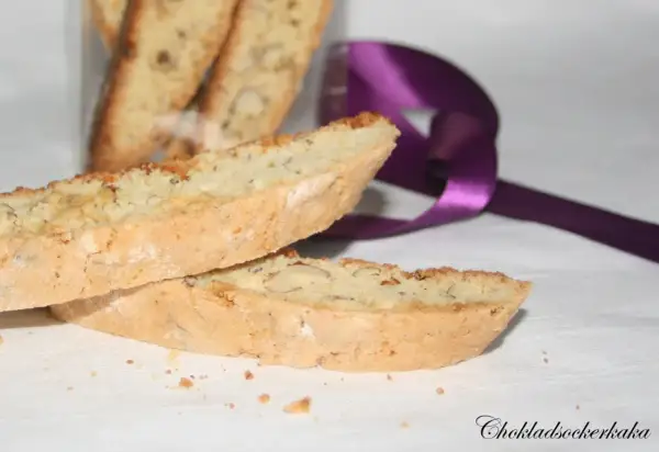 Två mandelkakor, perfekta för ditt biscotti recept, ligger på en vit duk. En lila sidenband ligger bakom.