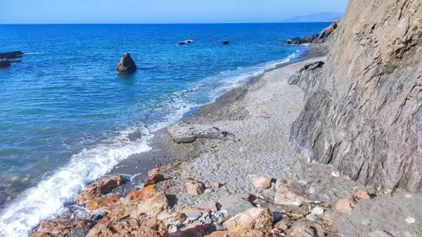 Costa de Almería, con sus guainos y rocas, el mar azul y las olas rompiendo en la playa de guijarros.
