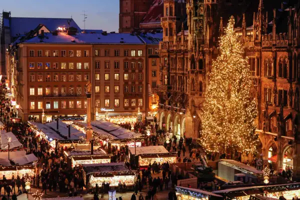 Beleuchteter Weihnachtsbaum und geschäftiger Weihnachtsmarkt bis Silvester, mit Buden und Menschen vor historischen Gebäuden.