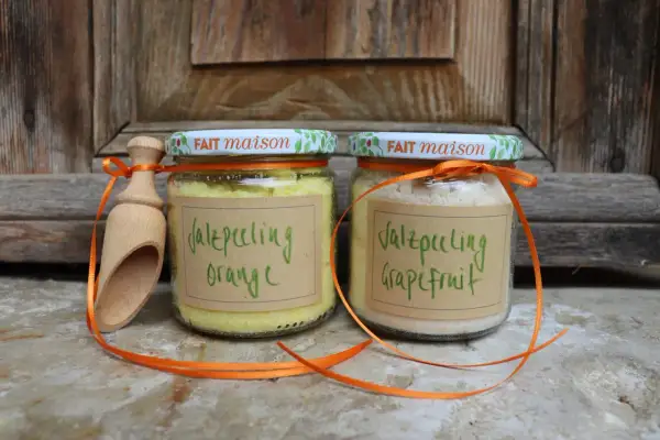 Zwei Gläser mit selbstgemachtem Saunasalz (Orange & Grapefruit) und eine Holzschaufel, verziert mit orangefarbenen Bändern.