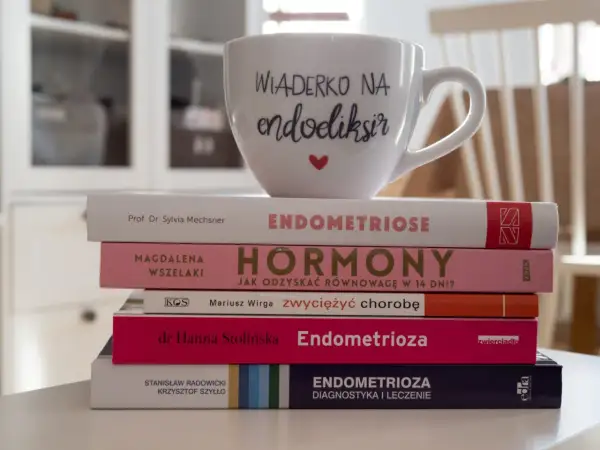 Stos książek o endometriozie, w tym "Endometrioza: diagnostyka i leczenie", z kubkiem "Wiaderko na endoeliksir".