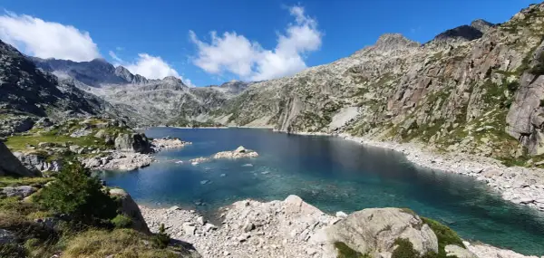 Lago azul cristalino en el corazón del Vall de Boí Aigüestortes, rodeado de imponentes montañas rocosas y vegetación escasa.