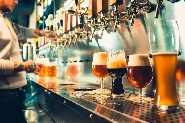 Vari tipi di bicchieri e il loro uso per degustare birre artigianali. Un barista con tatuaggi serve una birra dorata.