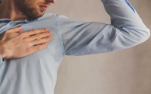 Hombre con camisa azul mostrando manchas de sudor bajo el brazo. Una solución para quitar manchas de sudor es necesaria.