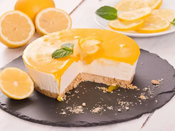 Ein Anschnitt eines cremigen Lemon Cheesecake mit Zitronenscheiben und Minze garniert.
